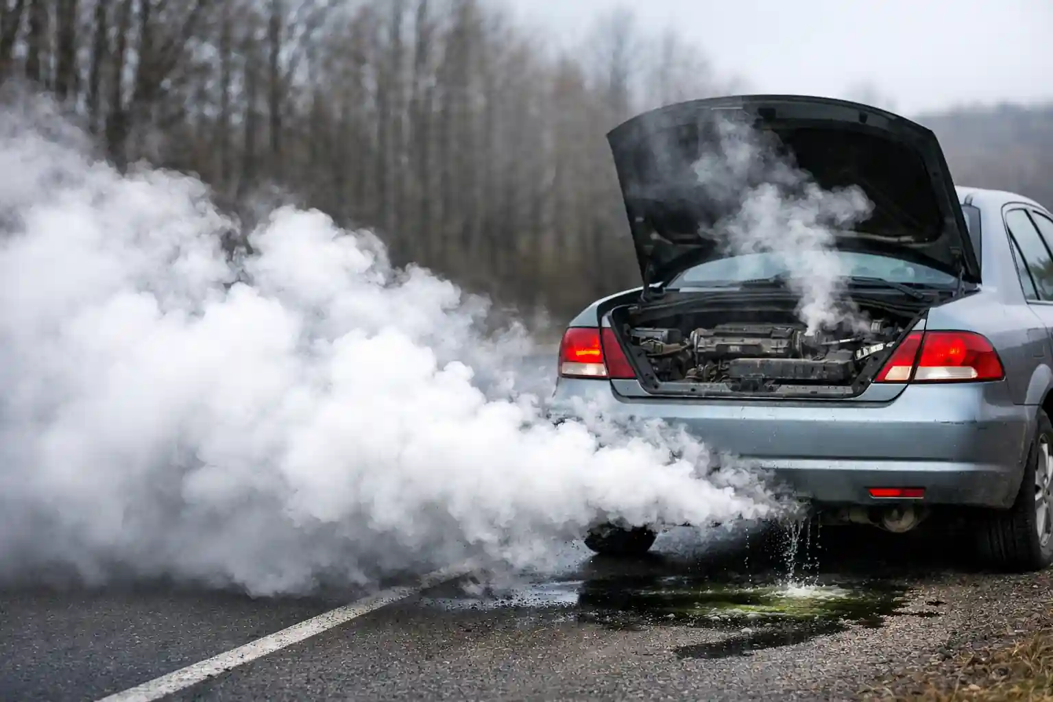 fumée blanche persistante sortant de l’échappement d’une voiture en panne avec capot ouvert et fuite de liquide de refroidissement sur la route